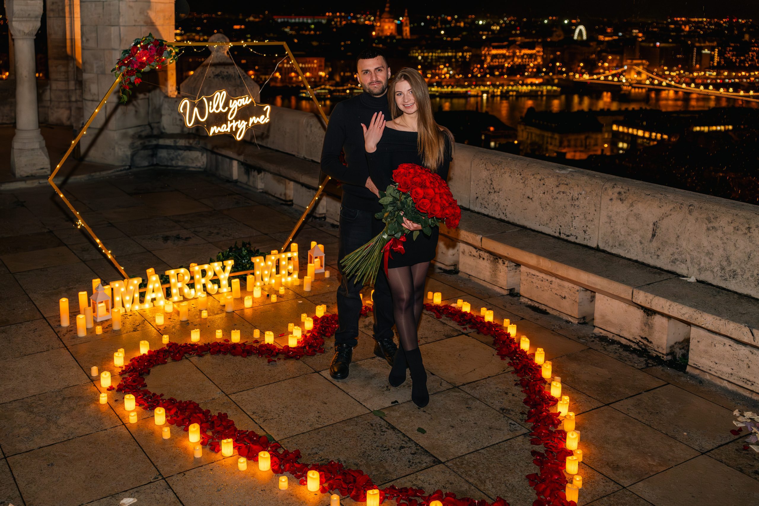 couple embracing during a candlelit proposal at Fisherman’s Bastion in Budapest at night. {{brizy_dc_image_alt imageSrc=