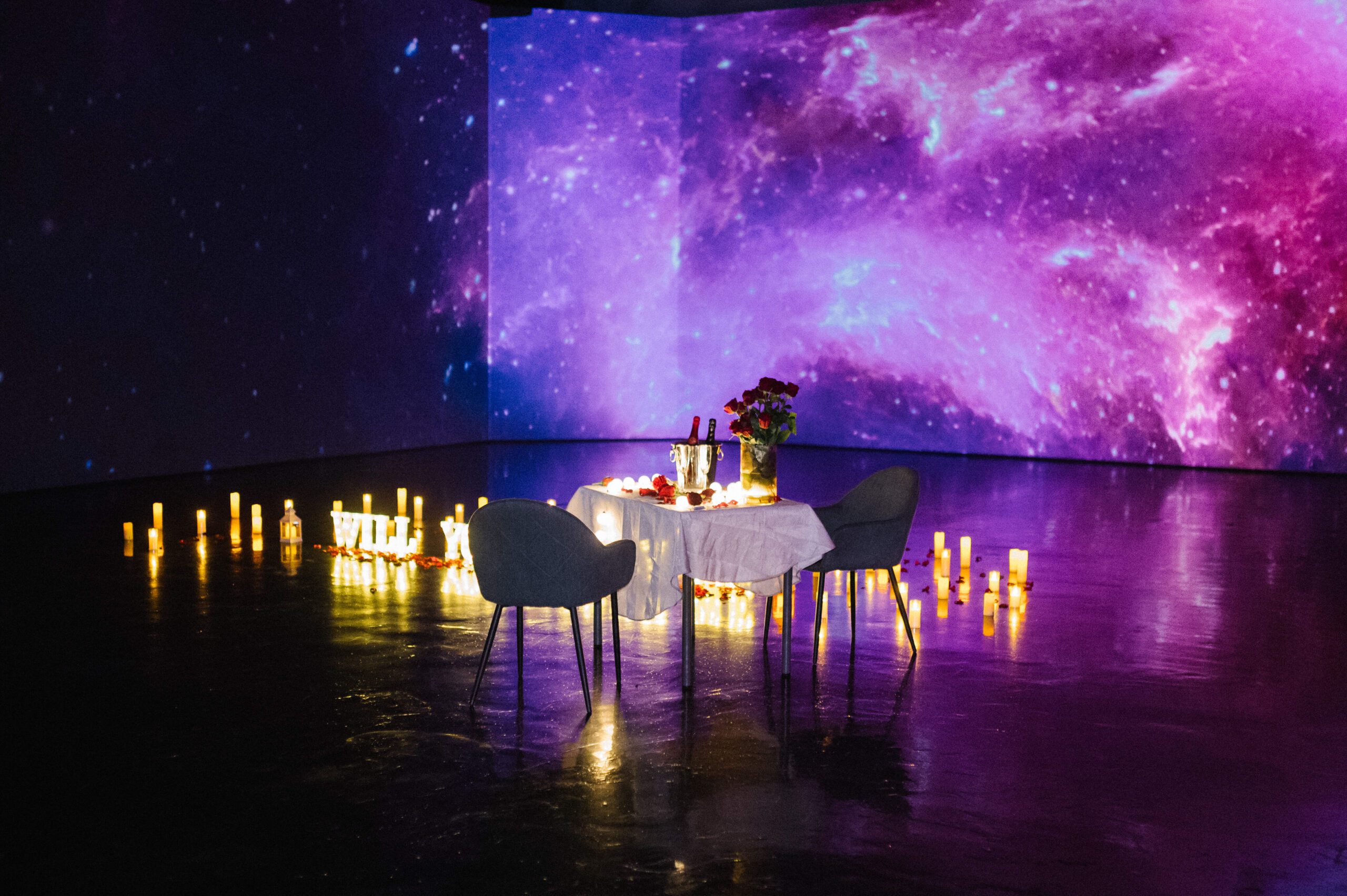 Romantic private proposal setup in a multimedia room in Budapest, featuring candles, roses, and a galaxy-themed background. {{brizy_dc_image_alt imageSrc=