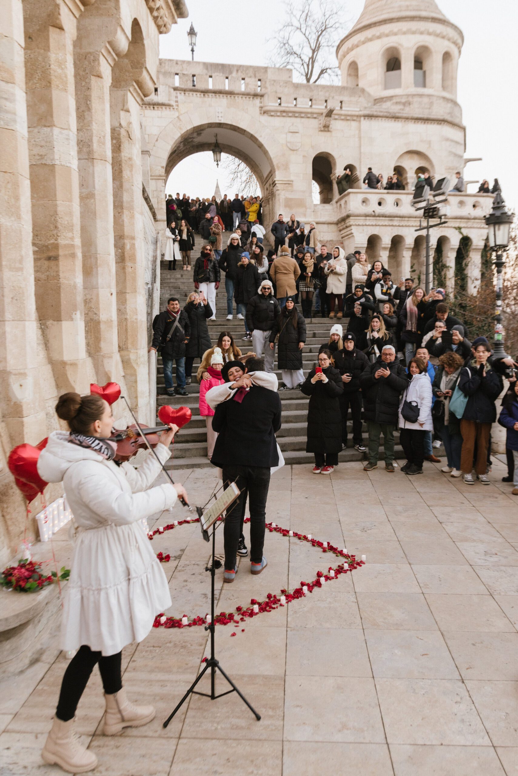 Engagement moment at Fisherman’s Bastion, with a couple celebrating the proposal surrounded by friends and tourists {{brizy_dc_image_alt imageSrc=