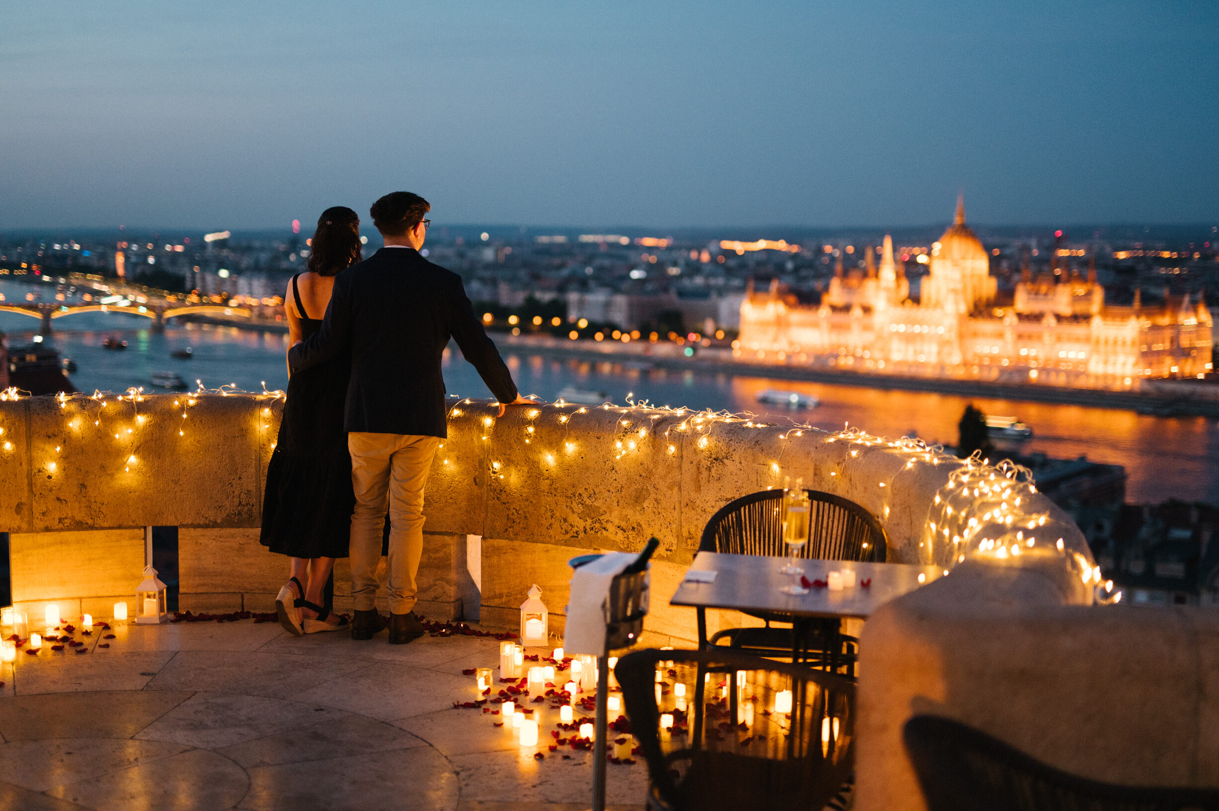 Fisherman's Bastion proposal on the private terrace, with a view of the illuminated Hungarian Parliament and candles surrounding the couple {{brizy_dc_image_alt imageSrc=