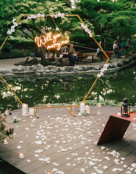 Proposal setup with a 'Will you marry me?' neon sign, candles, and flower petals at Margaret Island