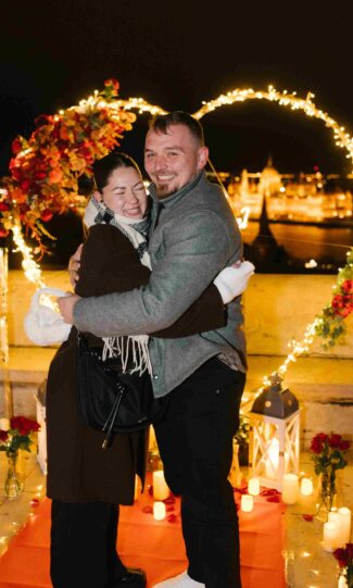 Happy couple embracing after a romantic proposal at Fisherman’s Bastion in Budapest, surrounded by candles and a glowing heart decoration {{brizy_dc_image_alt imageSrc=