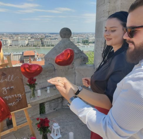 Close-up of a couple's engagement at Fisherman's Bastion in Budapest, with a 'Will you marry me?' sign and romantic red heart balloons