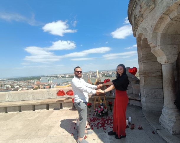 Couple celebrating their engagement at Fisherman's Bastion in Budapest, surrounded by heart-shaped balloons, flowers, and rose petals