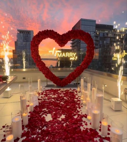 Luxurious rooftop marriage proposal setup with a heart-shaped rose arrangement, candles, and cityscape view at sunset in Budapest, Hungary.