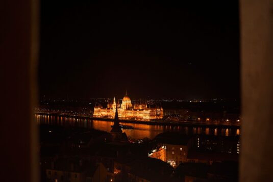 Night view of the illuminated Hungarian Parliament in Budapest from across the Danube River {{brizy_dc_image_alt imageSrc=