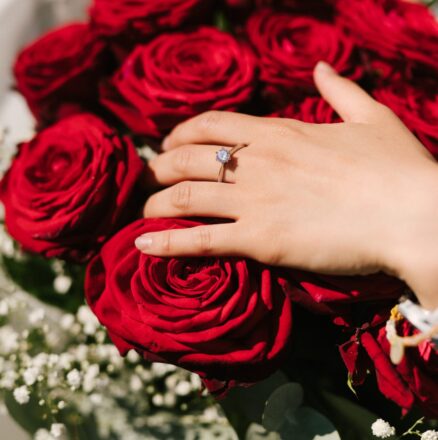 Közelkép egy eljegyzési gyűrűről egy nő kezén, amely egy vörös rózsacsokron nyugszik. {{brizy_dc_image_alt imageSrc=