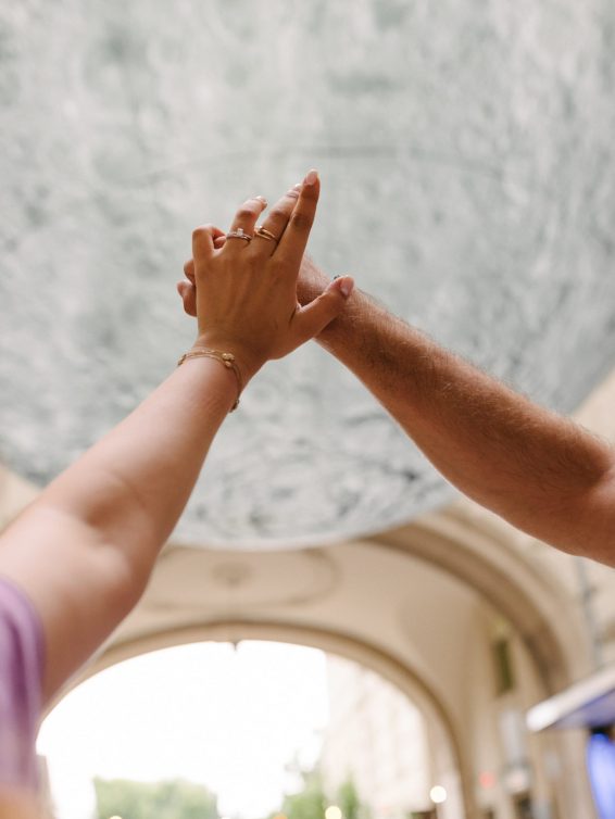 Close-up of a couple holding hands during a proposal in Budapest, with a moon installation in the background