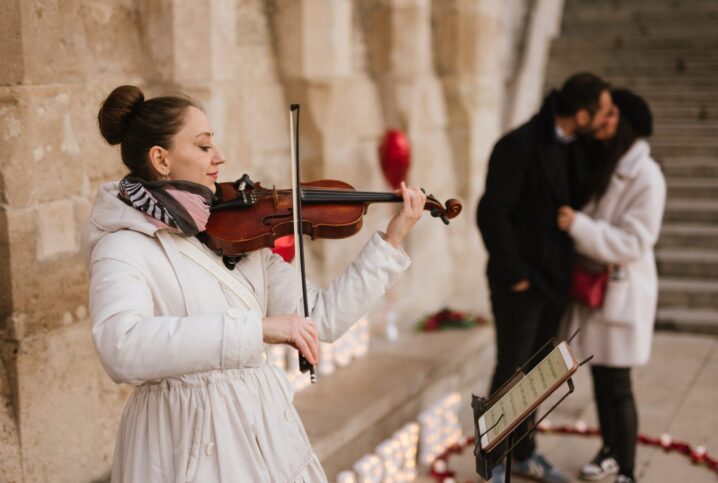 Violinist playing for a couple during an intimate and emotional marriage proposal in Budapest, with rose petals and heart-shaped decor {{brizy_dc_image_alt imageSrc=