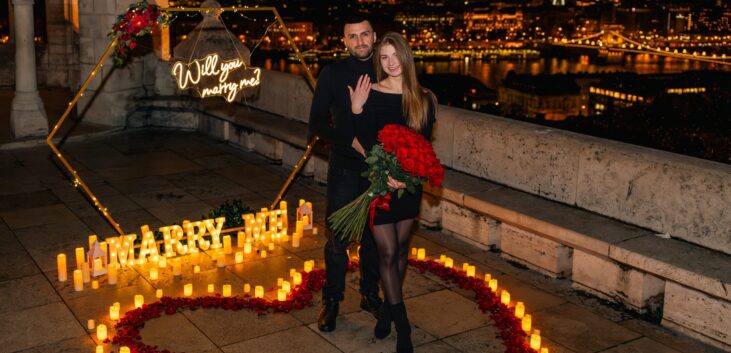 couple embracing during a candlelit proposal at Fisherman’s Bastion in Budapest at night. {{brizy_dc_image_alt imageSrc=