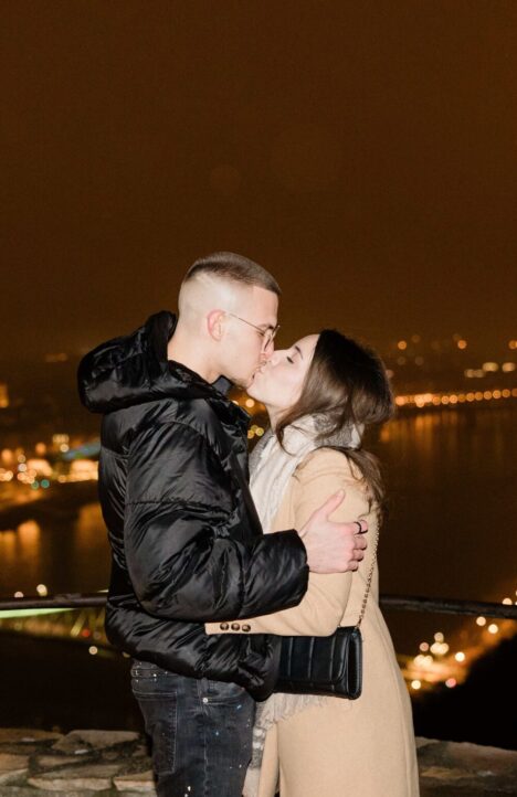 Couple kissing after a proposal above the Danube River and Liberty Bridge in Budapest, Hungary – romantic city night view {{brizy_dc_image_alt imageSrc=