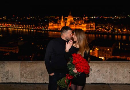 Romantic couple engagement with a bouquet of red roses at Fisherman’s Bastion, Budapest, overlooking the castle at night {{brizy_dc_image_alt imageSrc=