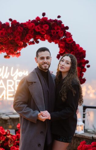 Engaged couple posing with engagement ring after proposal in Budapest with romantic rose heart arch {{brizy_dc_image_alt imageSrc=